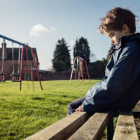 Upset problem child sitting on play park playground bench concept for bullying, depression, child protection or loneliness